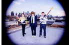 Download Foto: Drei Personen stehen auf einem Dach mit Instrumenten; im Hintergrund eine Skyline. Bild hat eine Vignette.