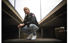 Download Foto: Eine Person mit langen Zöpfen hockt lässig unter einer Brücke, trägt eine schwarze Jacke und weiße Sneaker.