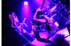 Download Foto: Zwei Musiker in auffälligen Outfits performen unter violettem Licht auf einer Bühne; einer spielt Gitarre, der andere Bass.
