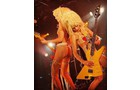Download Foto: Zwei Musiker mit blonder Lockenperücke spielen in knapper Kleidung auf E-Gitarren. Die Bühne ist in warmes Licht getaucht.