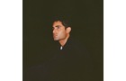 Download Foto: Ein Mann in dunkler Kleidung vor dunklem Hintergrund, im Profil nach rechts blickend.