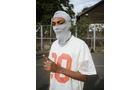 Download Foto: Jemand trägt eine weiße Maske und ein weißes T-Shirt mit roter '89'. Im Hintergrund sind Bäume und ein Zaun zu sehen.