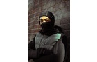 Download Foto: Person in dunkler Winterkleidung und Mütze, Gesicht teilweise verdeckt, lehnt an einer Backsteinwand mit verschränkten Armen.