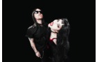 Download Foto: Zwei Personen in schwarzer Kleidung, eine trägt Sonnenbrille, die andere mit roten Lippenstift und gefärbtem Haar vor schwarzem Hintergrund.