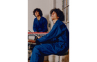 Download Foto: Zwei Personen in blauen Overalls sitzen in einem Raum, eine spielt ein elektrisches Keyboard.