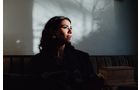 Download Foto: Eine Person sitzt im Schatten, Licht fällt dramatisch auf ihr Gesicht und erzeugt Schattenmuster an der Wand im Hintergrund.