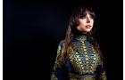 Download Foto: Frau mit langem, wallendem Haar in einem kunstvoll gemusterten, blau-goldenen Kleid vor einem dunklen Hintergrund.