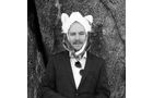 Download Foto: Ein Mann in Anzug und Krawatte steht vor einem Baum, trägt eine lustige Hutmaske mit Ohren, schwarz-weißes Foto.