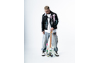 Download Foto: Mann in schwarzer Lederjacke und grauer Hose blickt auf eine bunte Gitarre, die er senkrecht hält. Weißer Hintergrund.