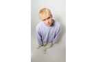 Download Foto: Ein blonder Mensch trägt einen hellblauen Pullover und weiße Hose, steht aufrecht und schaut aus der Vogelperspektive ernst in die Kamera.