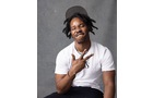 Download Foto: Ein Mann mit Dreadlocks und weißem T-Shirt sitzt vor einem grauen Hintergrund und zeigt mit den Fingern ein Peace-Zeichen.