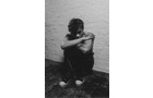 Download Foto: Schwarz-weiß-Foto einer Person, die in einer Ecke auf dem Boden sitzt, den Kopf auf die Knie gelegt und die Arme darum geschlungen hat.