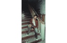 Download Foto: Ein Mann sitzt auf einer alten, hölzernen Treppe in einem düsteren, vernachlässigten Gebäude. Er trägt einen roten Mantel.