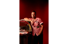Download Foto: Ein Mann in einem roten Hemd lehnt an einer nostalgischen Jukebox vor einem roten Hintergrund.