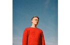 Download Foto: Eine Person in einem roten Pullover steht unter einem klaren blauen Himmel und blickt in die Ferne.