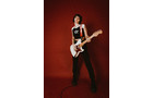 Download Foto: Person mit schwarzem Outfit spielt E-Gitarre vor einem roten Hintergrund.