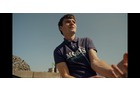 Download Foto: Ein Mann in einem blauen Poloshirt sitzt im Freien unter klarem Himmel und schaut in die Ferne. Er wirkt entspannt und nachdenklich.