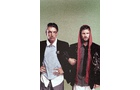 Download Foto: Zwei Männer stehen zusammen. Der linke trägt einen schwarzen Blazer, der rechte hat ein rotes Tuch über dem Kopf. Hintergrund ist grün.