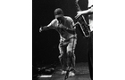 Download Foto: Ein Mann tanzt auf einer Bühne, während eine andere Person ein Saxofon spielt. Die Szene ist in Schwarzweiß gehalten.