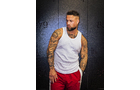 Download Foto: Ein Mann mit Tattoos trägt ein weißes Tanktop und rote Hosen. Er steht vor einem dunklen Hintergrund und schaut zur Seite.