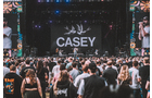 Download Foto: Eine Menschenmenge steht vor einer Bühne, auf der 'CASEY' und zwei Vögel auf einem großen Bildschirm zu sehen sind.