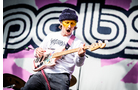 Download Foto: Person auf einer Bühne trägt eine Tiermaske und spielt eine E-Gitarre vor einem bunten Hintergrund.