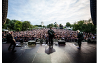 Download Foto: Blick von der Bühne auf eine große Menschenmenge bei einem Open-Air-Konzert im Freien, Musiker spielen im Vordergrund.
