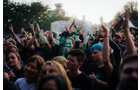 Download Foto: Eine fröhliche Menschenmenge bei einem Konzert im Freien, einige Personen klatschen, eine Person trägt auffälliges Kostüm.