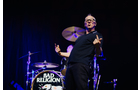 Download Foto: Eine Person singt leidenschaftlich auf der Bühne vor einem Schlagzeug mit 'Bad Religion'-Logo. Bühne dunkel mit blauem Licht.