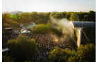 Download Foto: Großes Freiluftkonzert in einem Park. Eine dichte Menschenmenge steht vor einer Bühne, während Wasser zur Kühlung versprüht wird.