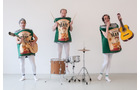 Download Foto: Drei Personen in Chipstüten-Kostümen spielen Instrumente, Gitarre und Schlagzeug, vor weißem Hintergrund.