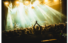 Download Foto: Eine Menschenmenge bei einem Konzert, bunte Lichter scheinen auf die Bühne, Hände klatschen, stimmungsvolle Atmosphäre.