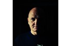 Download Foto: Mann mit Glatze, starker Schatten auf der rechten Gesichtshälfte, dunkler Hintergrund. Beleuchtung betont Gesichtszüge.