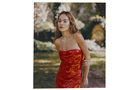 Download Foto: Person in einem schulterfreien roten Kleid steht draußen, umgeben von unscharfer grüner und blumiger Kulisse.