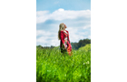Download Foto: Eine Frau in einem roten Kleid steht in einem grünen Feld, den Kopf zum Himmel gewandt, umgeben von blauem Himmel mit Wolken.