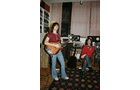 Download Foto: Zwei Personen in einem Raum mit musikalischem Equipment. Eine steht mit Gitarre, die andere sitzt. Gemütliche, kreative Atmosphäre.