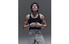 Download Foto: Person in gestreifter Hose und schwarzem Tanktop schaut nach oben, Arme leicht gebeugt. Hintergrund neutral grau.