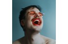 Download Foto: Person mit roten Lippenstift und orange getönter Brille lacht in einem blauen Hintergrund.