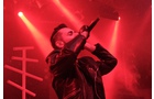 Download Foto: Ein Sänger performt mit Mikrofon auf einer Bühne, umgeben von intensiv rotem Licht und Nebel, trägt eine schwarze Lederjacke.