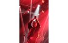 Download Foto: Eine Person steht auf einer Bühne im roten Licht, klatscht und ist von Scheinwerfern umgeben.