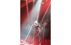 Download Foto: Ein Sänger steht auf einer Bühne, singt in ein Mikrofon. Rotes und weißes Bühnenlicht strahlt von oben herab.