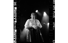 Download Foto: Schwarz-weiß-Foto einer Person auf der Bühne, die in ein Mikrofon singt. Bühnenbeleuchtung im Hintergrund.