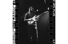 Download Foto: Schwarz-weiß-Foto einer Person, die E-Gitarre spielt, umgeben von Bühnenlicht, mit einem Filmstreifen-Rand.