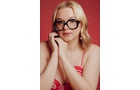Download Foto: Eine Person mit blonden Haaren und großer Brille schaut nachdenklich. Sie trägt ein rotes Oberteil vor einem roten Hintergrund.