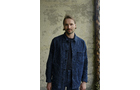 Download Foto: Ein Mann in einer blauen Jeansjacke steht vor einer verwitterten Wand und schaut geradeaus.