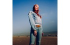 Download Foto: Eine Person steht in einem hellen Jeans-Outfit auf offenem Feld bei blauem Himmel.