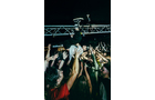 Download Foto: Eine Person surft auf Händen der Menge bei einem Konzert, umgeben von begeisterten Menschen unter einer dunklen Beleuchtung.