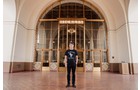 Download Foto: Eine Person steht in einer großen Halle mit hohen Decken und großen Glastüren im Hintergrund.