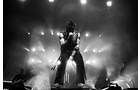 Download Foto: Schwarz-weiß-Foto eines Sängers auf einer Bühne mit grellen Lichtern und Rauch, der in ein Mikrofon singt.