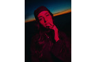 Download Foto: Person mit Mütze in rotem Licht, Hand am Gesicht, dunkler Hintergrund mit blauem Himmel und orangefarbenem Horizontstreifen.